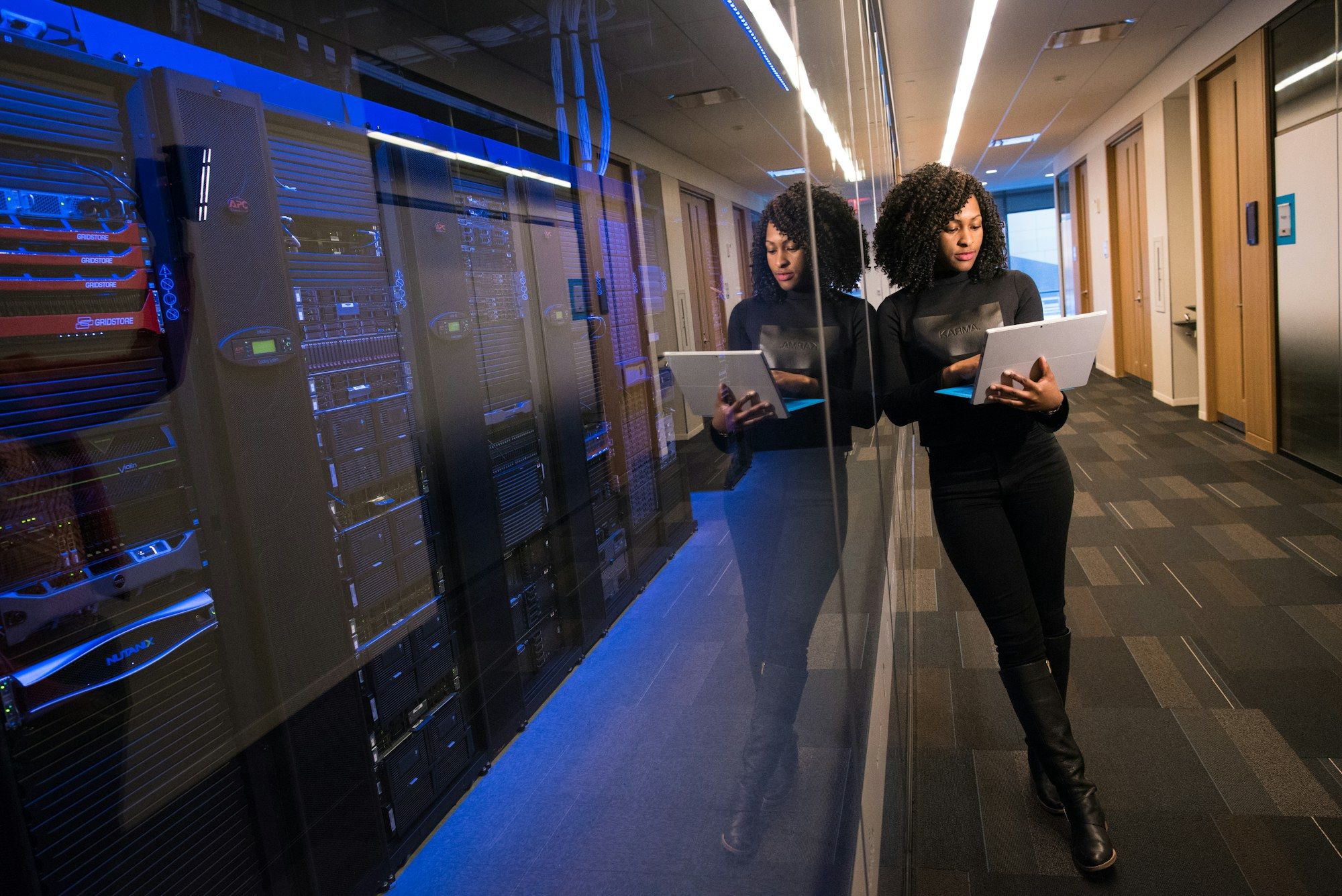 Two engineers with laptops reviewing a row of server racks in a data hall